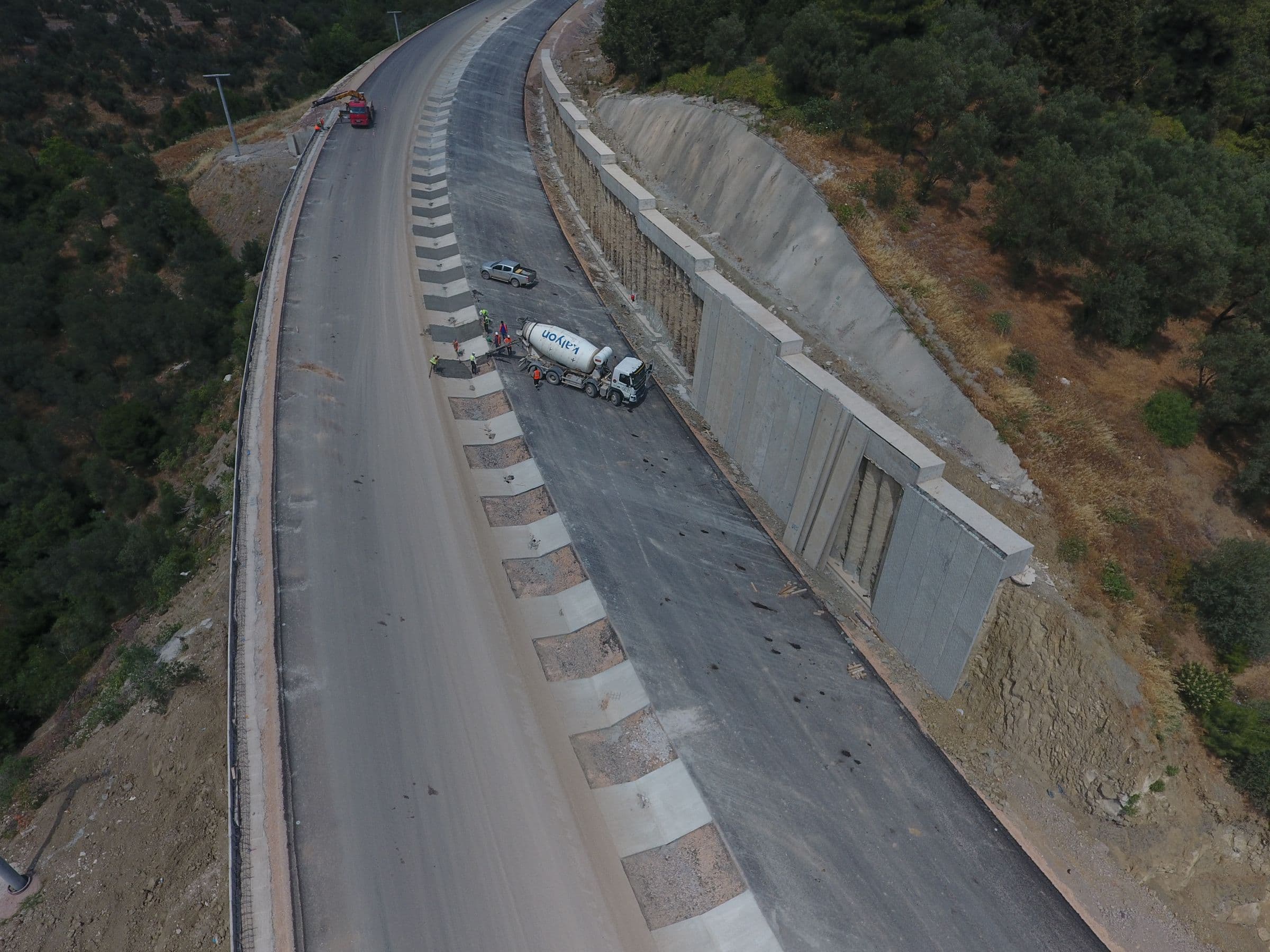 Aerial view of a new mountain road under construction alongside a concrete retaining wall.