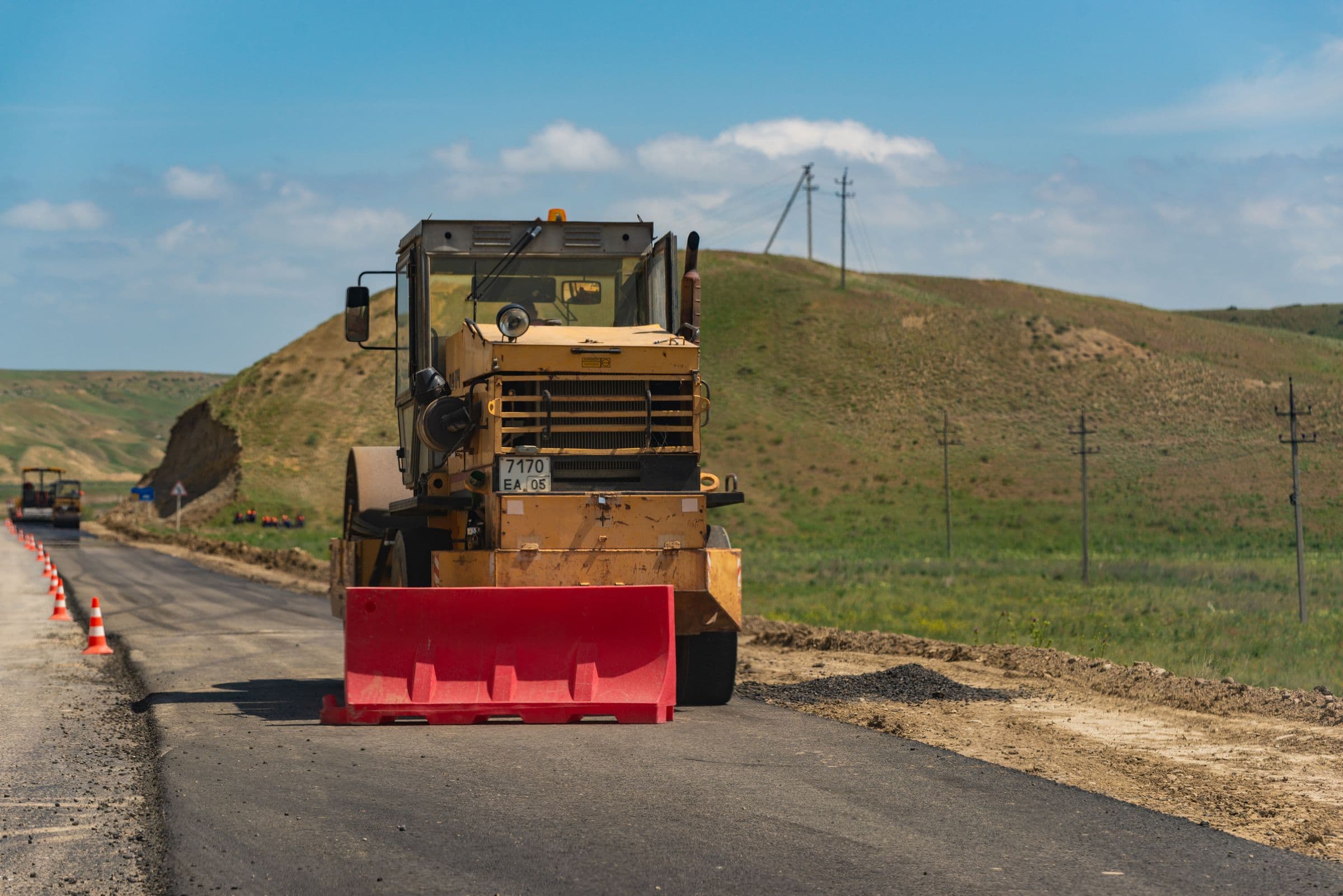 A roller compacting the base layer of a rural road under construction.