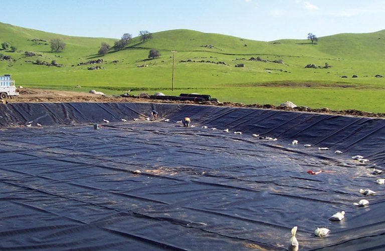 Géomembrane déroulée et lestée sur le fond et les talus d'un bassin de rétention